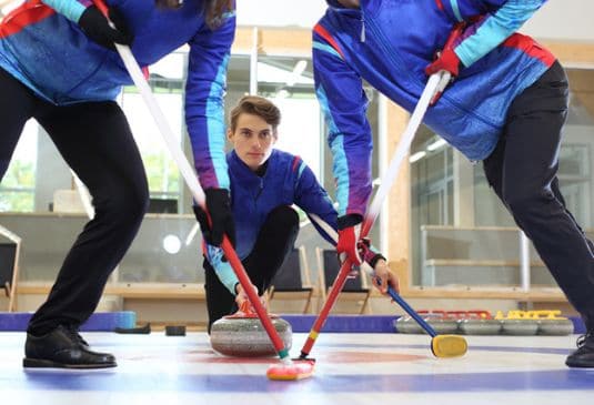 3 curling players sweeping the stone