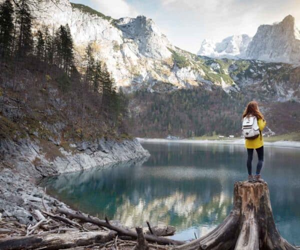 woman standing on tree stump beside a lake
