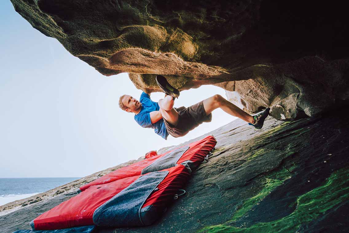 Man bouldering on overhanging rock with mat below