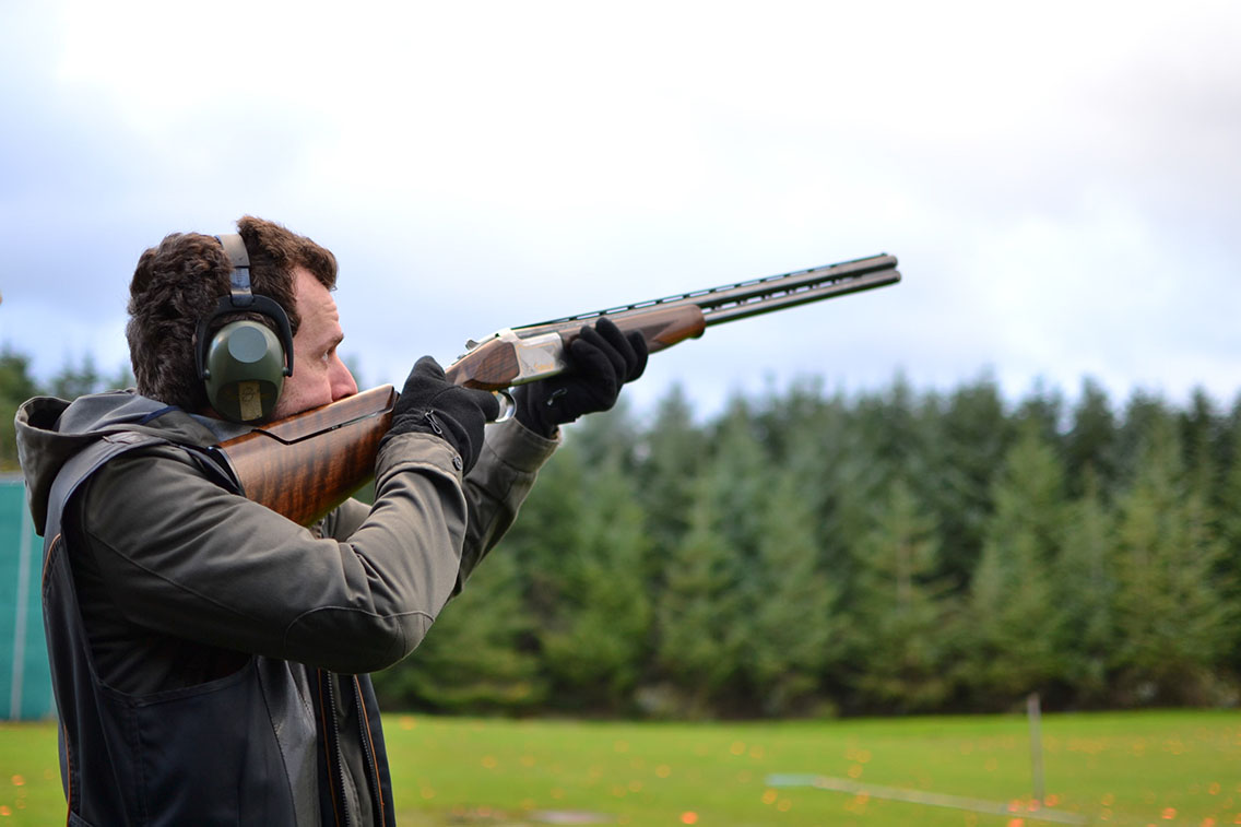 Man with shotgun and ear defenders in field