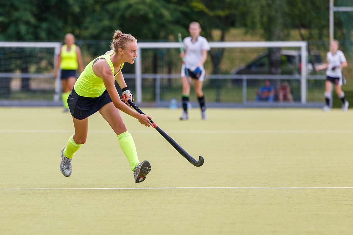 Girl running with hockey stick on pitch
