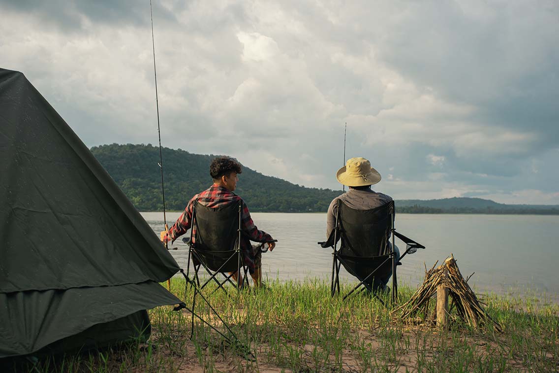 2 men sitting by lake with fishing equipment