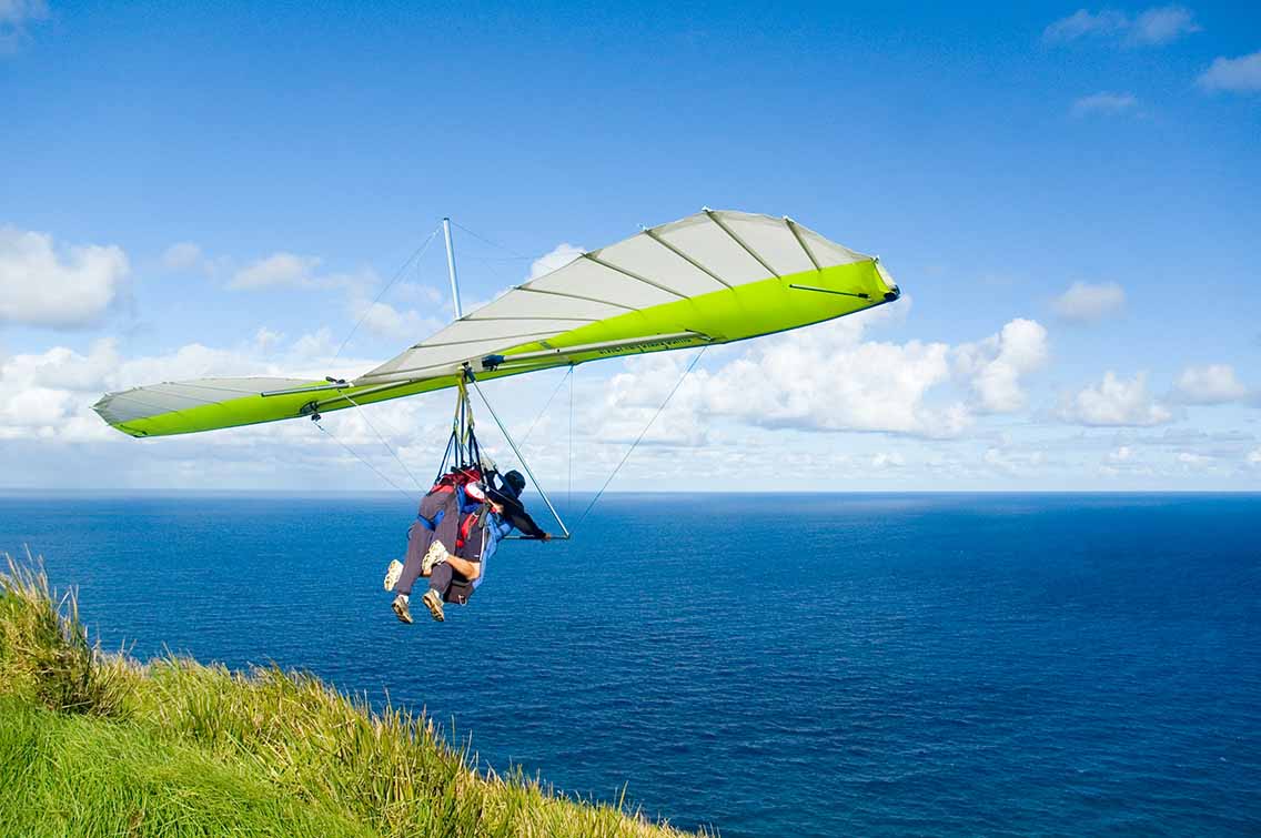 Tandem glider taking off cliff beside sea