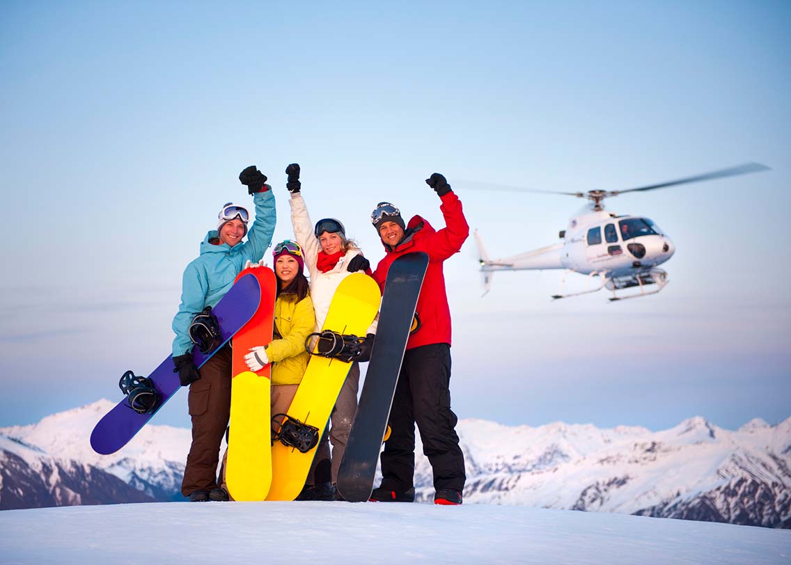 Snowboarders in front of helicopter on mountain