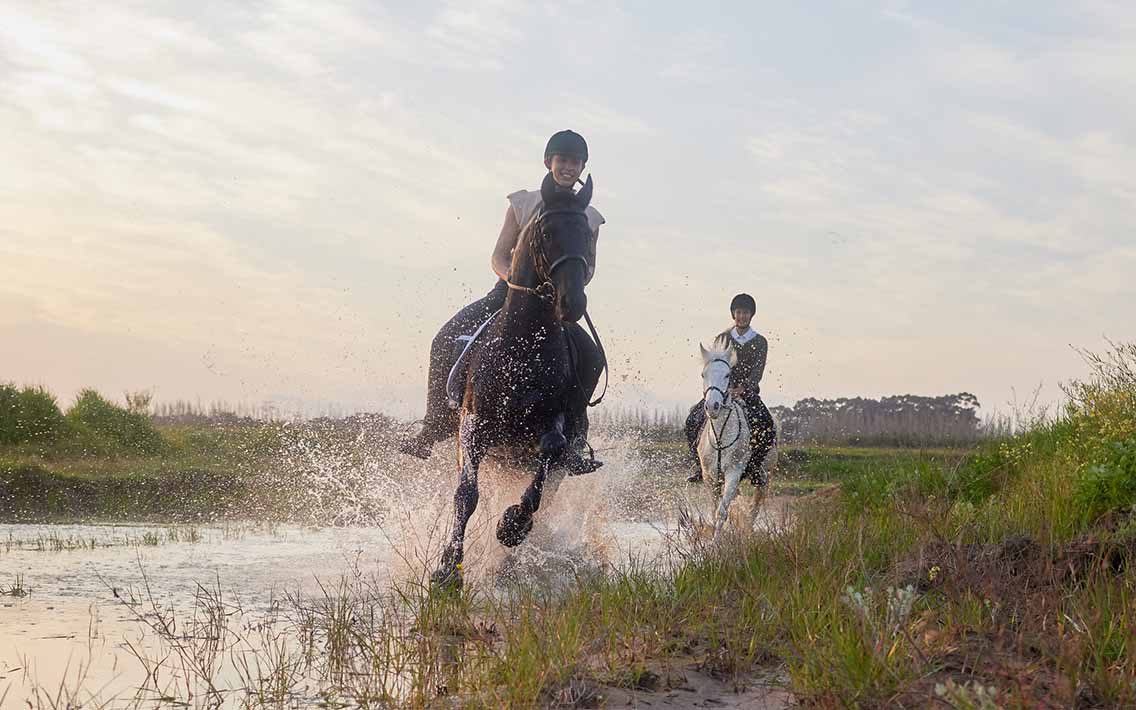 2 horse riders galloping through water