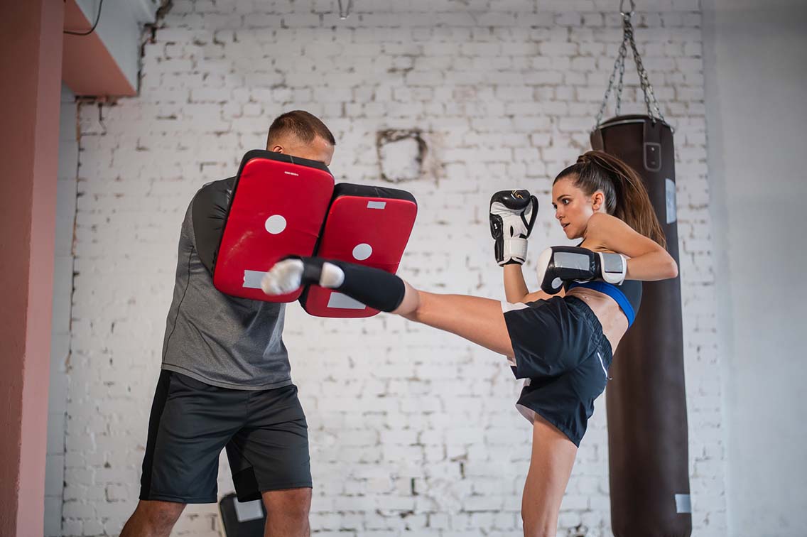 Female kickboxer kicking pads with trainer