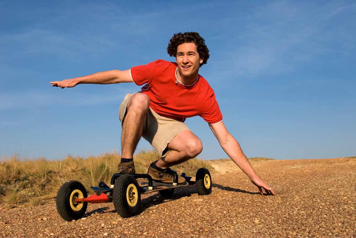 Man crouching on mountainboard riding down slope