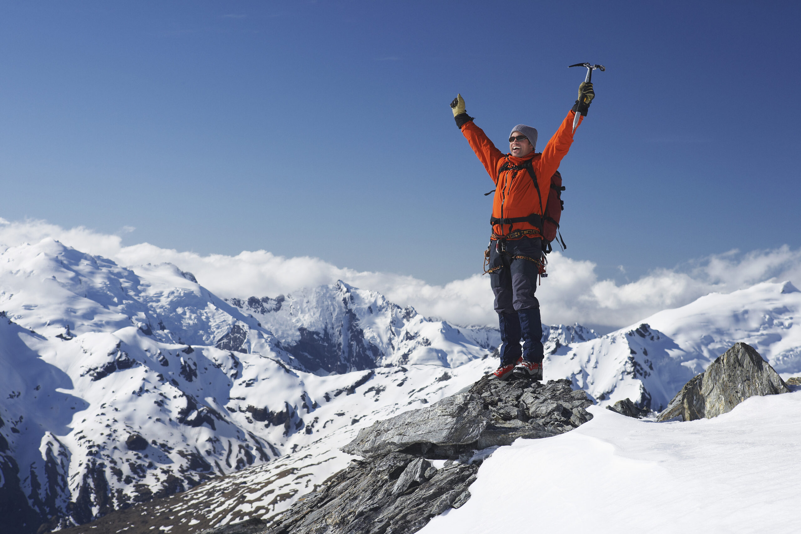Man at peak of snow capped mountains with mountaineering gear