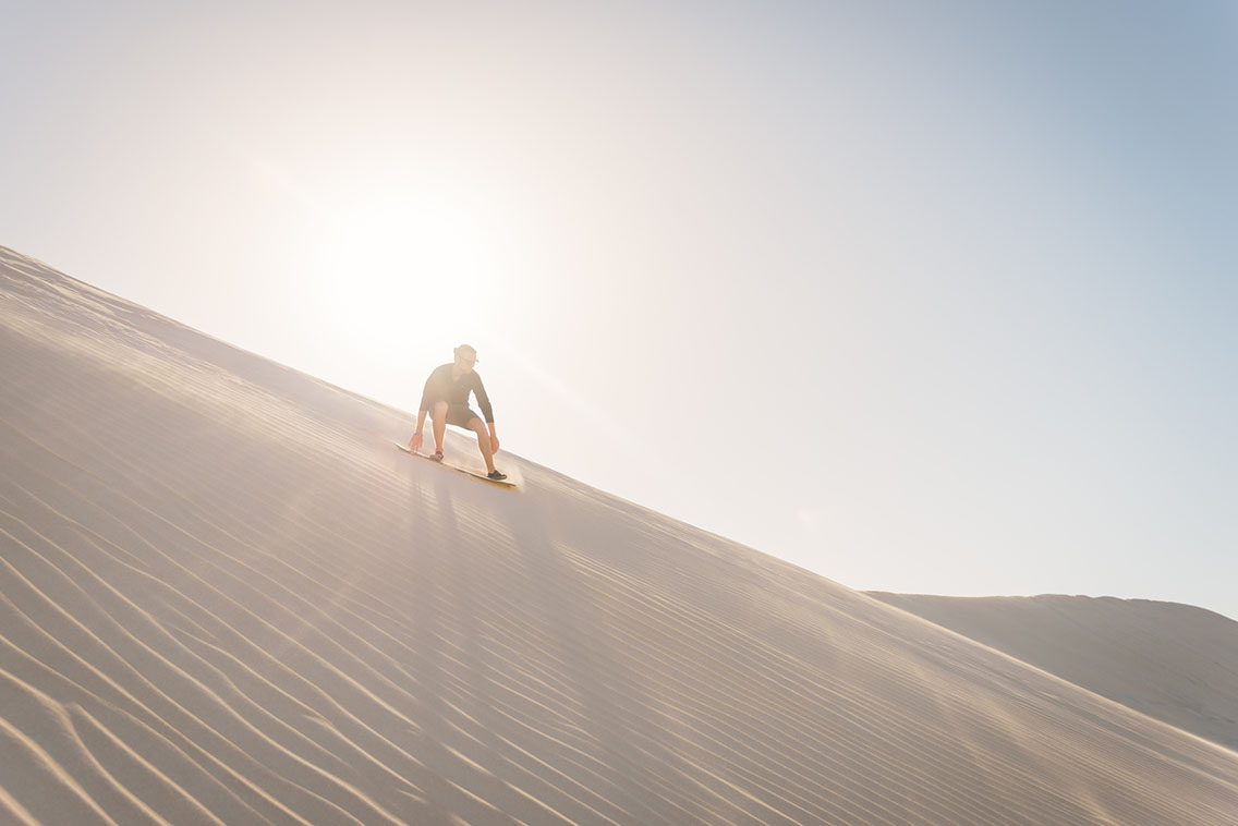 Man riding sandboard on sandy slope