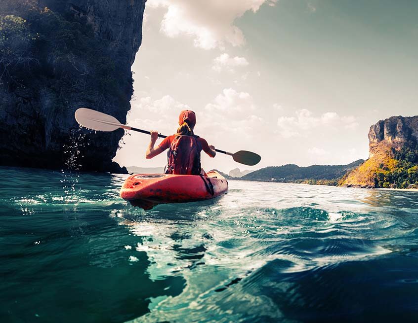 Woman kayaking on coastal water beside cliffs