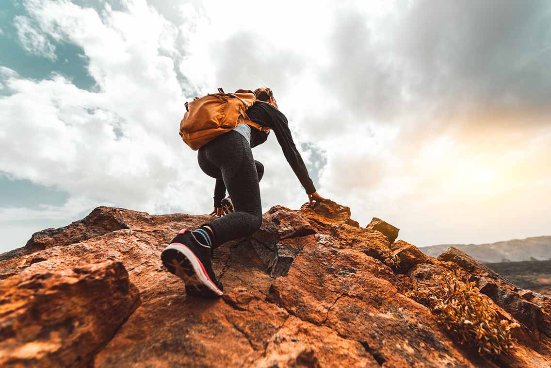 Woman scrambling up peak