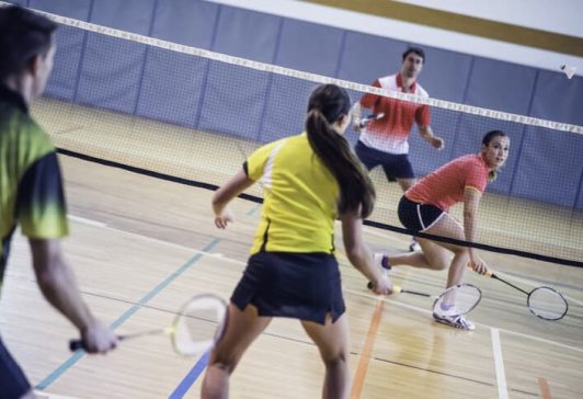 Rear view of two couples playing badminton against each other on an indoor court.