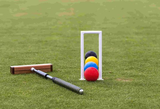 croquet mallet, wicket and colorful balls on a green lawn