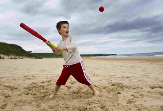 Little boy playing baseball on beach