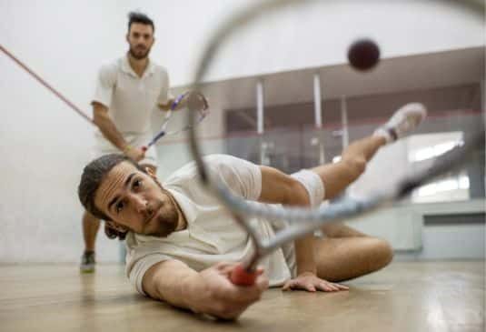 Young man playing squash with his friend while trying to catch a ball.