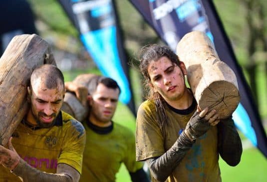 Obstacle race runners carrying a wooden trunk